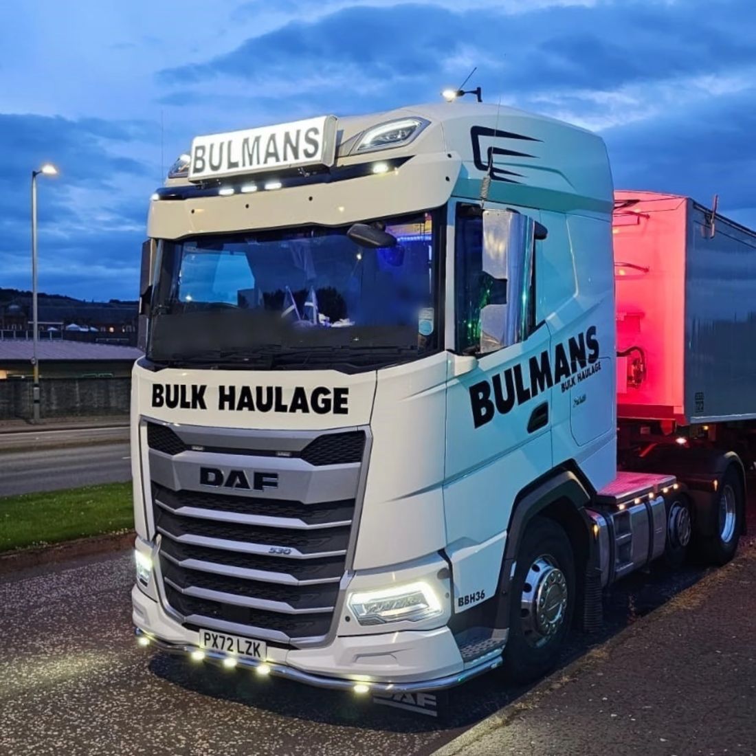A Bulmans Bulk Haulage DAF Truck parked on the side of the road at dusk, with a dark blue, cloudy sky overhead and street lights lighting the truck.
