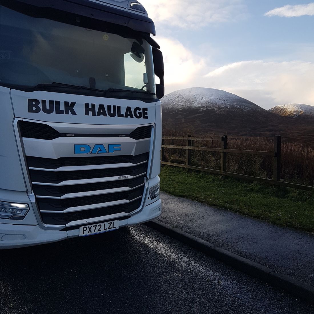 Close up of a Bulmans Bulk Haulage DAF truck cab, with snowy mountain peaks of the Lake District in the background.