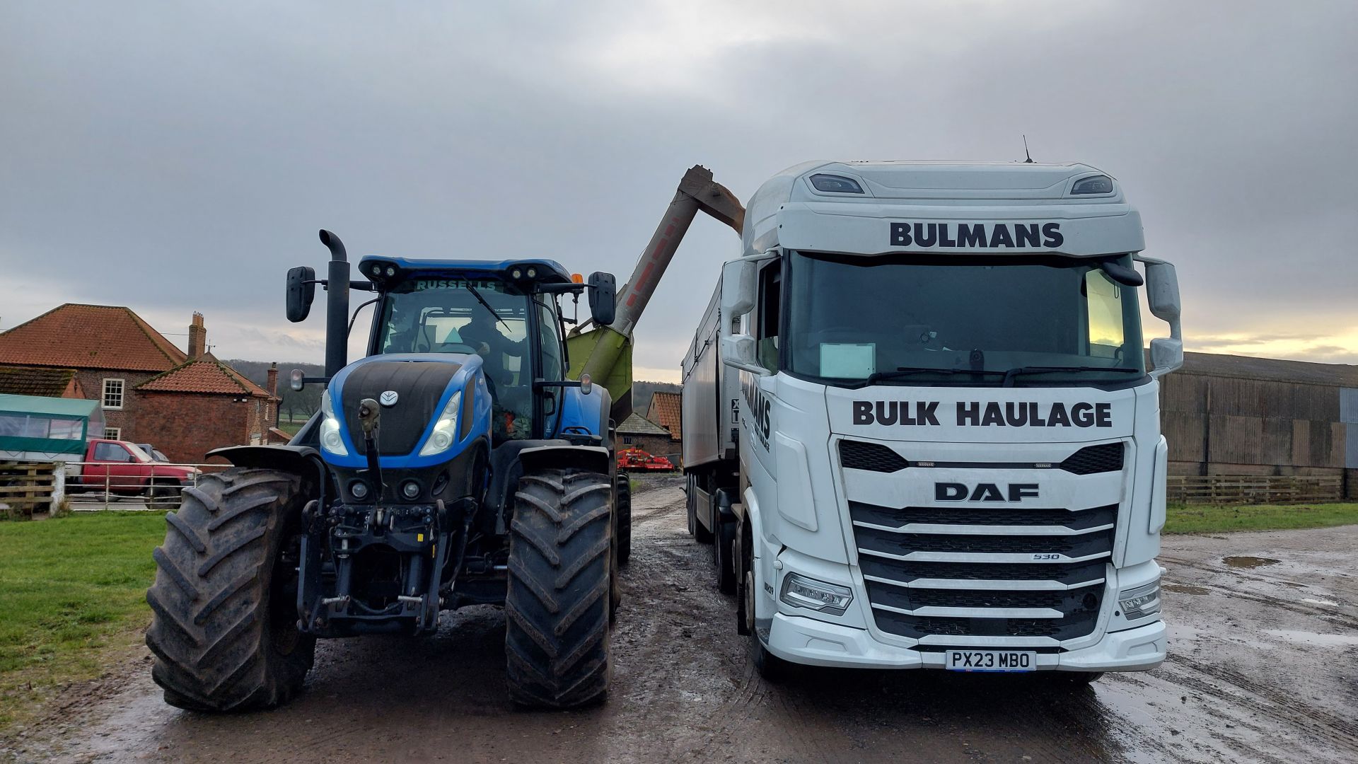 A Bulmans Bulk Haulage DAF truck is being loaded by a blue tractor on a farm.