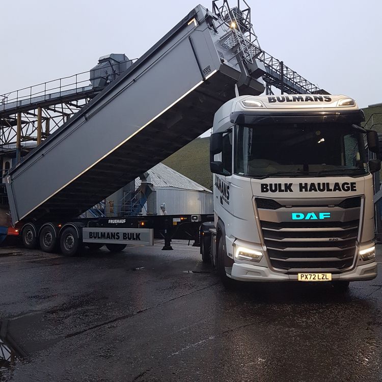 A Bulmans Bulk Haulage DAF Tipper Truck is unloading with its bulk tipper trailer raised, against a backdrop of industrial equipment.